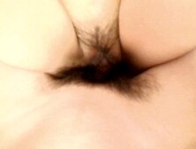 An Asian woman of mature age, with a pubic area covered in hair, playfully arouses him in anticipati